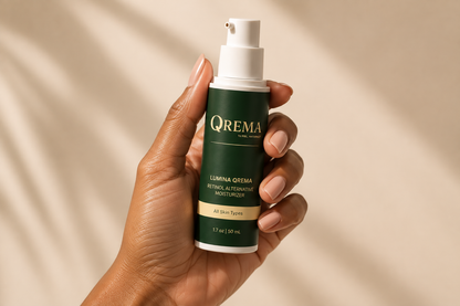 A hand holding a bottle of QREMA Lumina Orema Retinol Alternating Moisturizer against a warm beige background with soft leaf shadows.