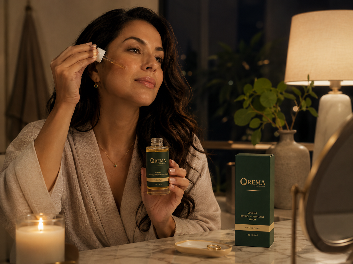 A woman in a beige robe applies skincare dropper cream to her face while holding a bottle of QREMA skincare serum. A green QREMA product box sits on the marble counter next to a lit candle and a mirror in a warmly lit, cozy room.